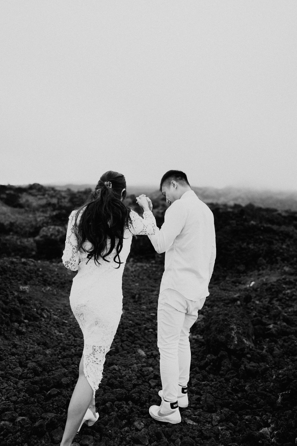 Black and white photo of two people in white outfits walking on volcanic rocks.