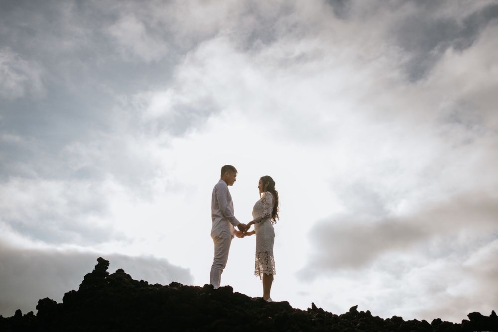 Silhouettes of a couple against dramatic cloudy sky on rocky terrain.