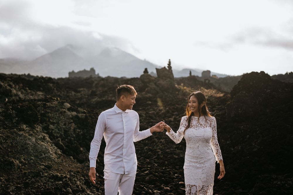 Two people in white clothing exploring a volcanic landscape under cloudy skies.