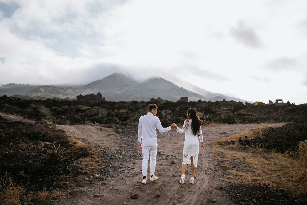 Two people in white clothing walking hand in hand on a mountain path.