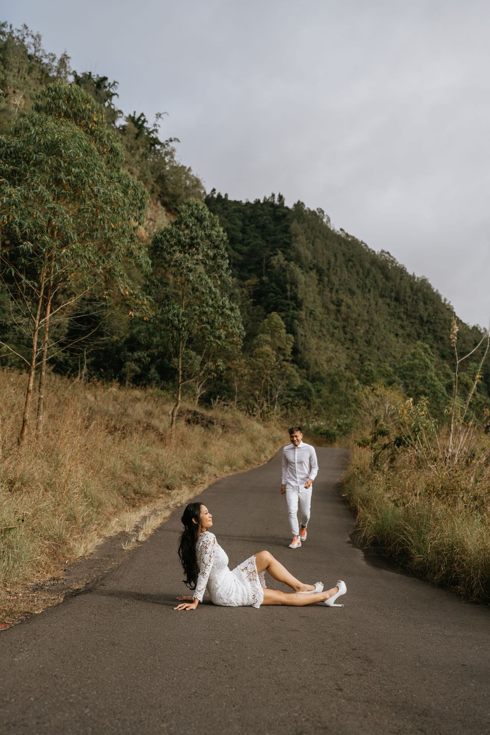 A couple in white clothing sitting casually on a curved mountain road.