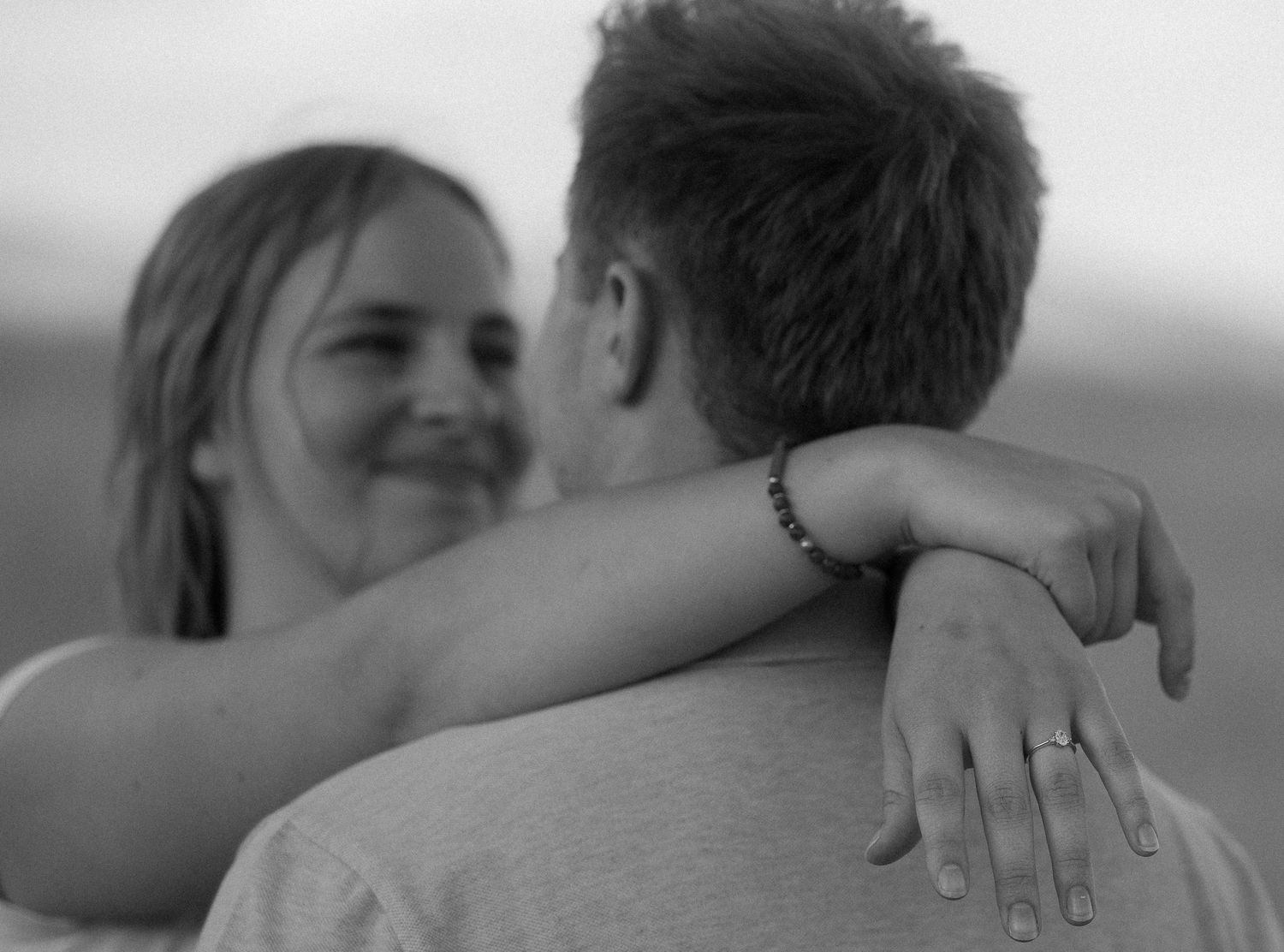 Engaged couple laughing and embracing in a sunlit outdoor portrait in Logan, UT.