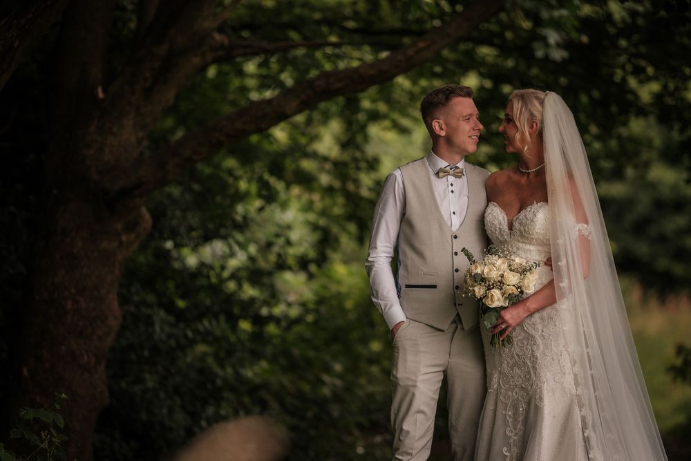 Newlywed couple embraces outdoors during a summer garden wedding ceremony wearing ivory and beige attire.