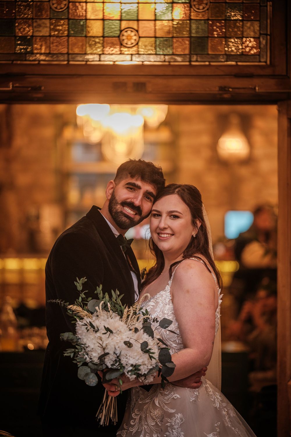 A couple shares a romantic moment in a warmly lit venue with ornate stained glass in the background.
