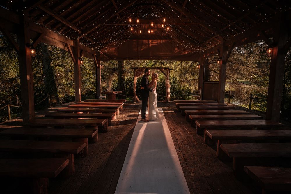 Outdoor chapel with wooden pews and tall trees creating a natural cathedral ceiling in a forest setting.