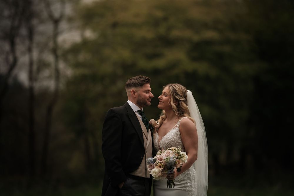 A romantic outdoor wedding scene captured at dusk in a natural wooded setting with soft lighting.