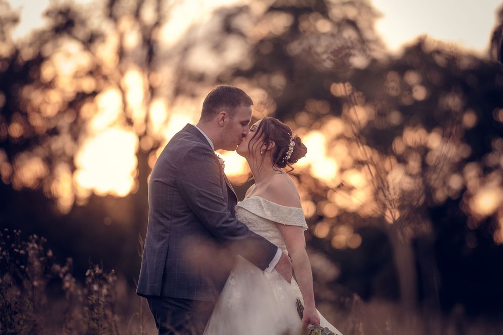 A romantic couple embraces during sunset as silhouettes against a warm golden sky in a scenic outdoor setting.