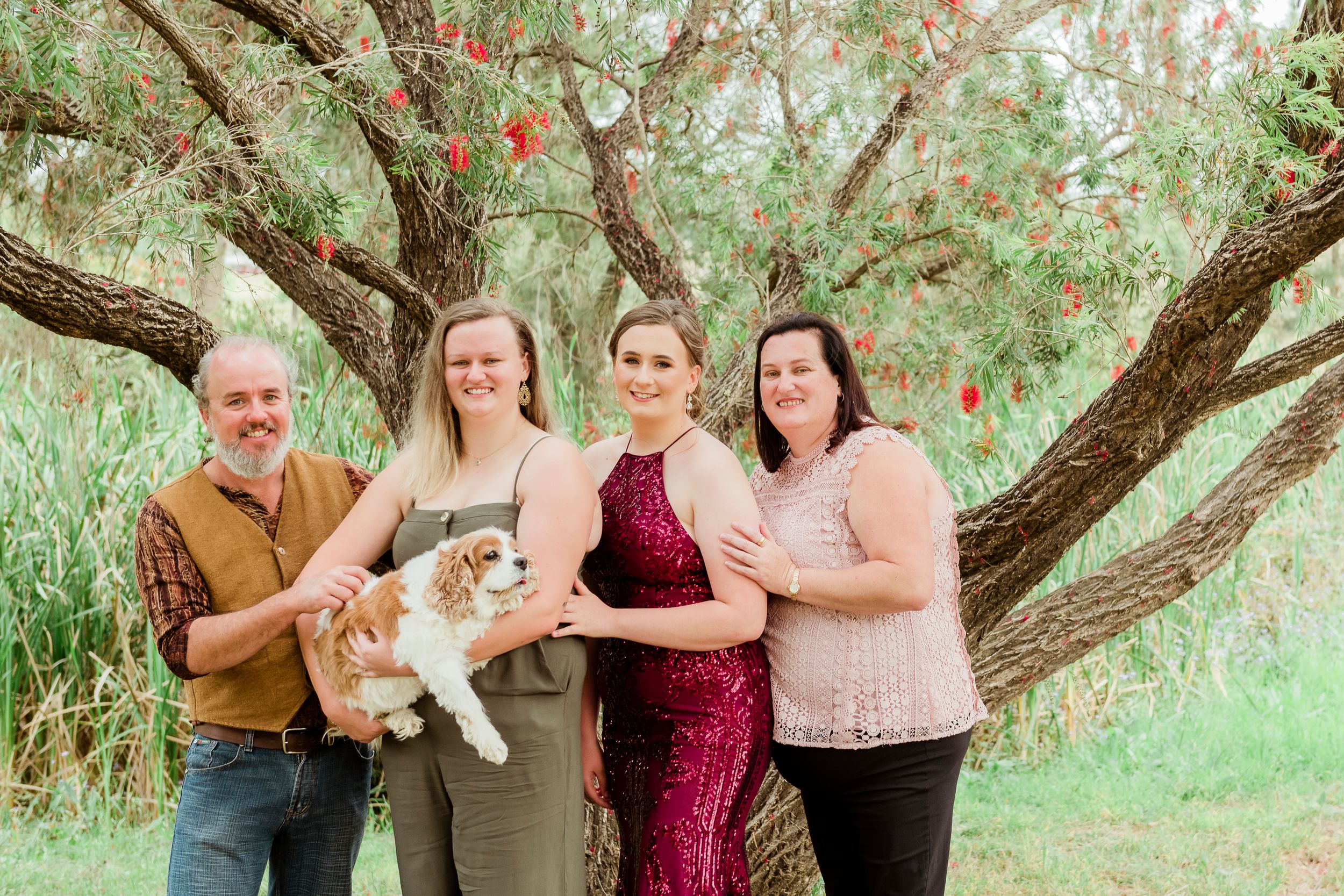 Family group portrait under flowering tree branches in garden setting.
