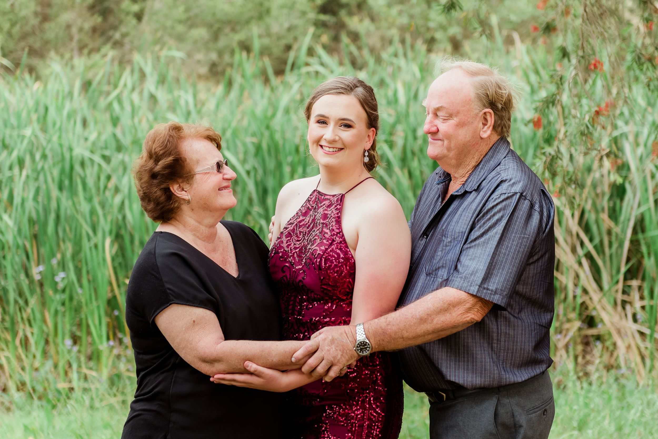 Three people share a joyful moment together in front of tall green grass during an outdoor photoshoot.