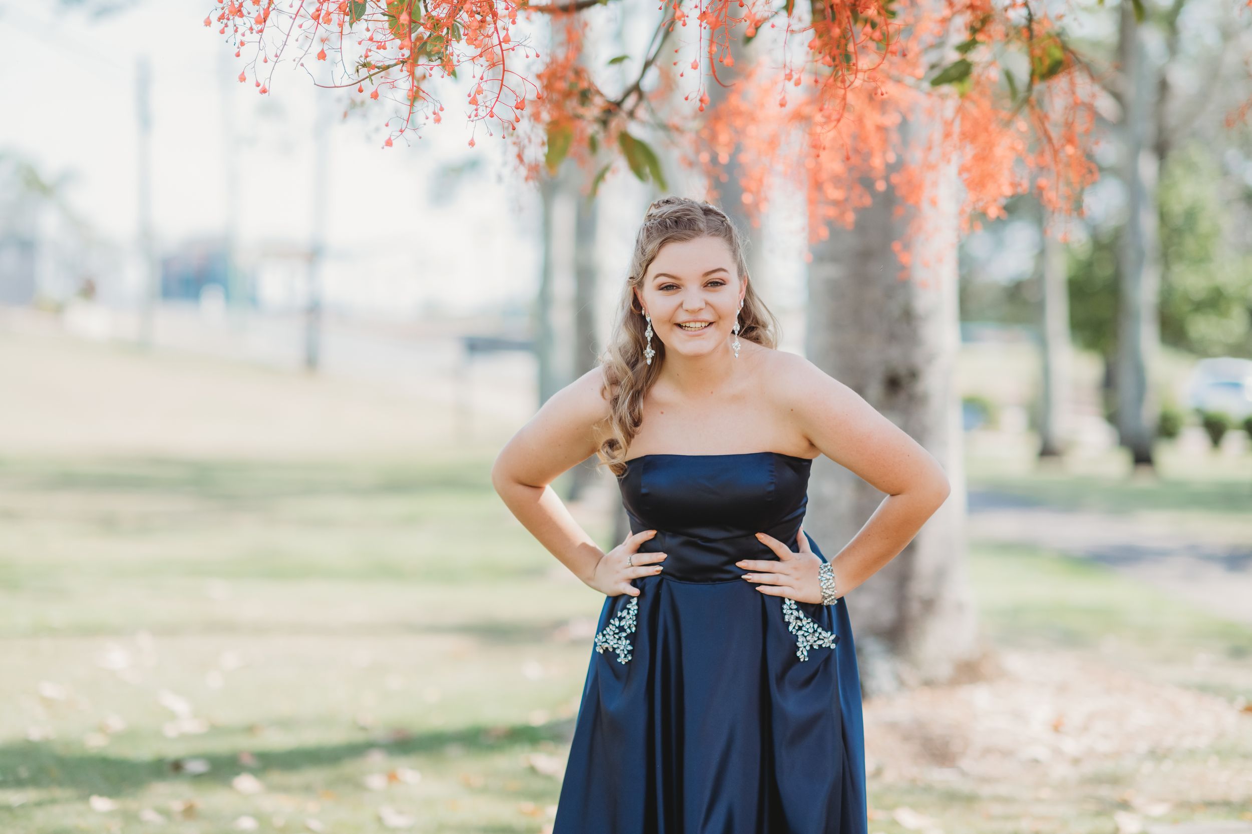 Person in a navy blue formal dress poses outdoors under flowering pink blossoms.