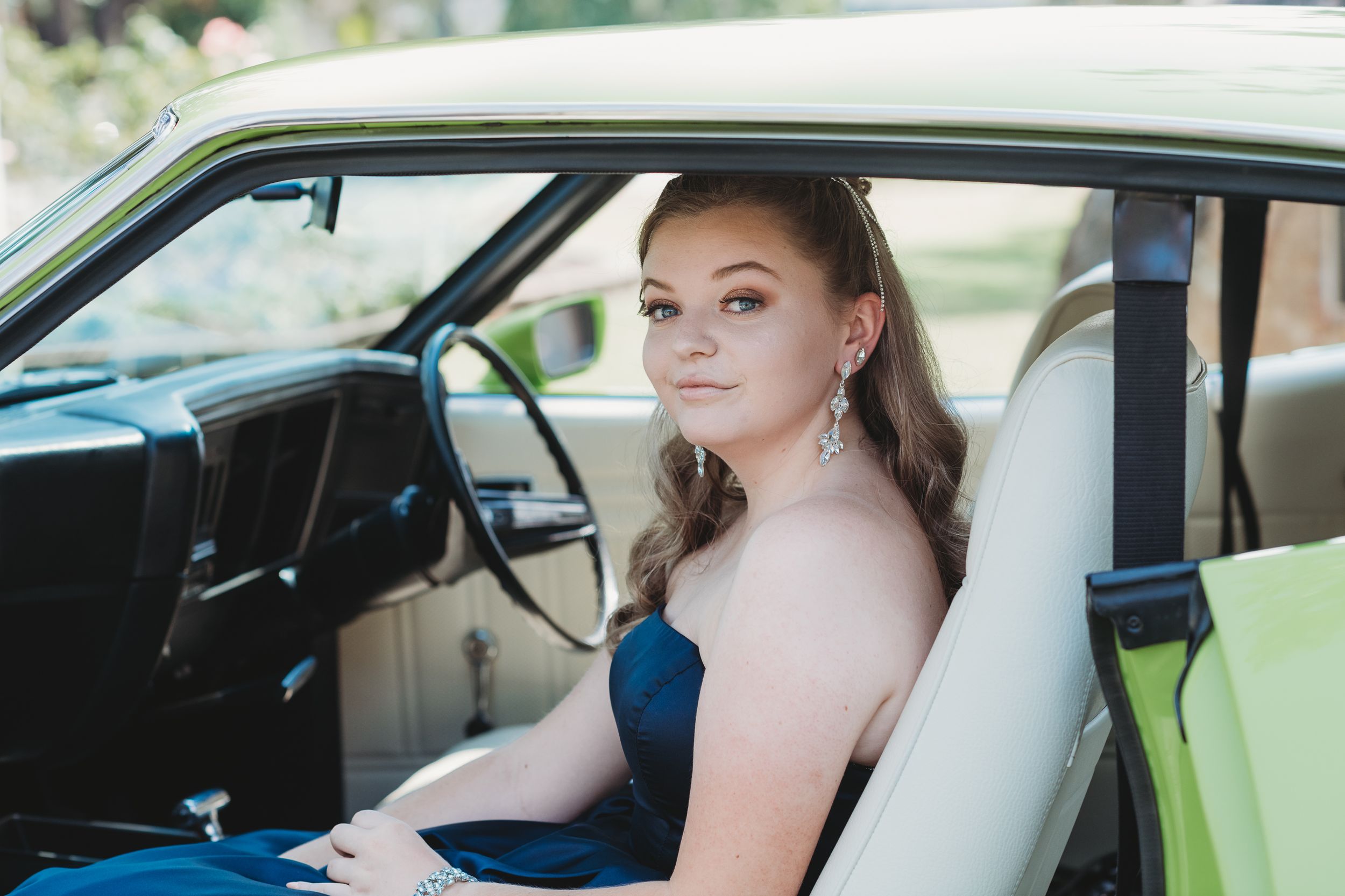 Person wearing blue dress poses inside a vintage car with white interior.