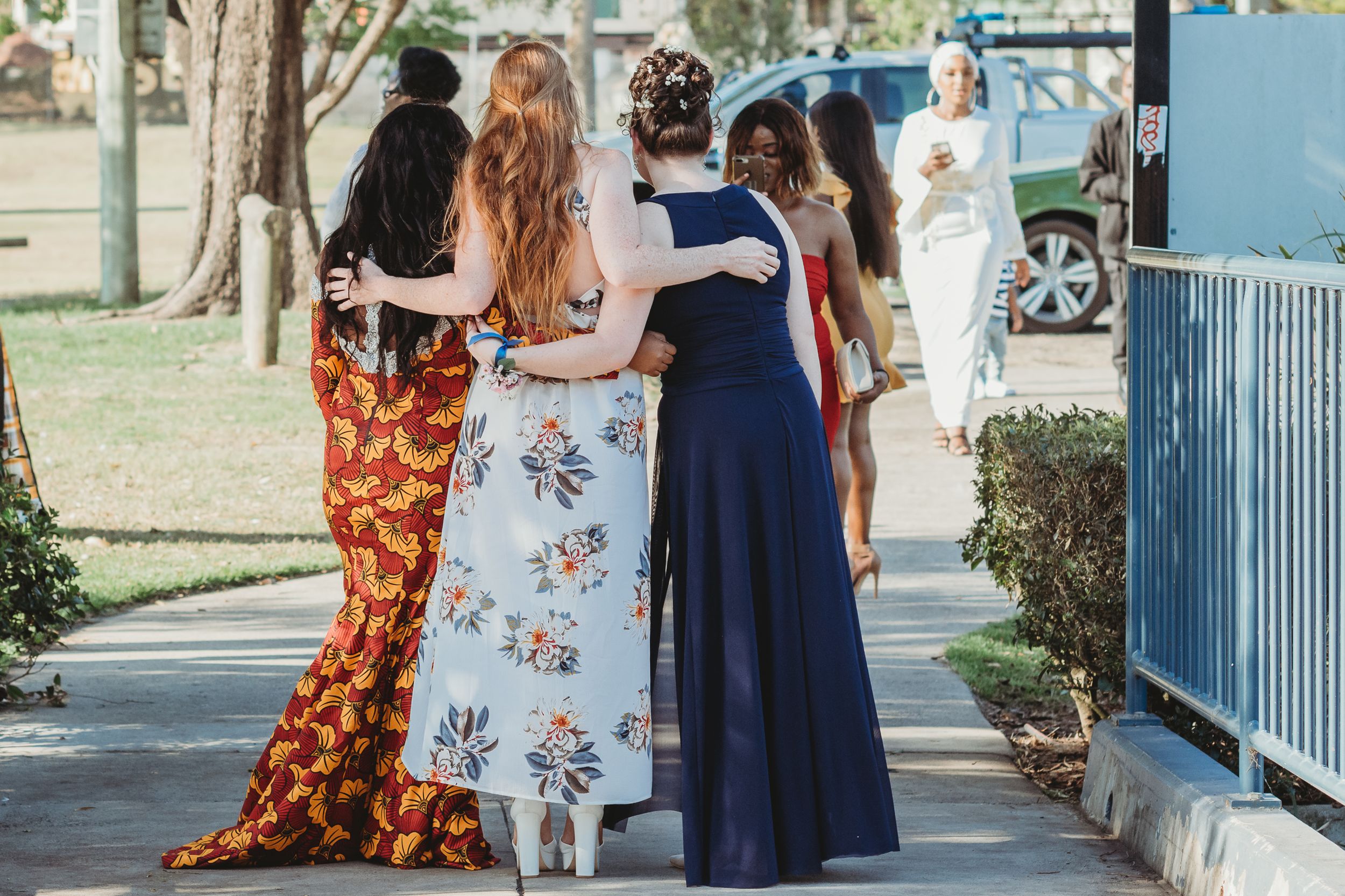 Friends walking together outdoors wearing colorful formal dresses.