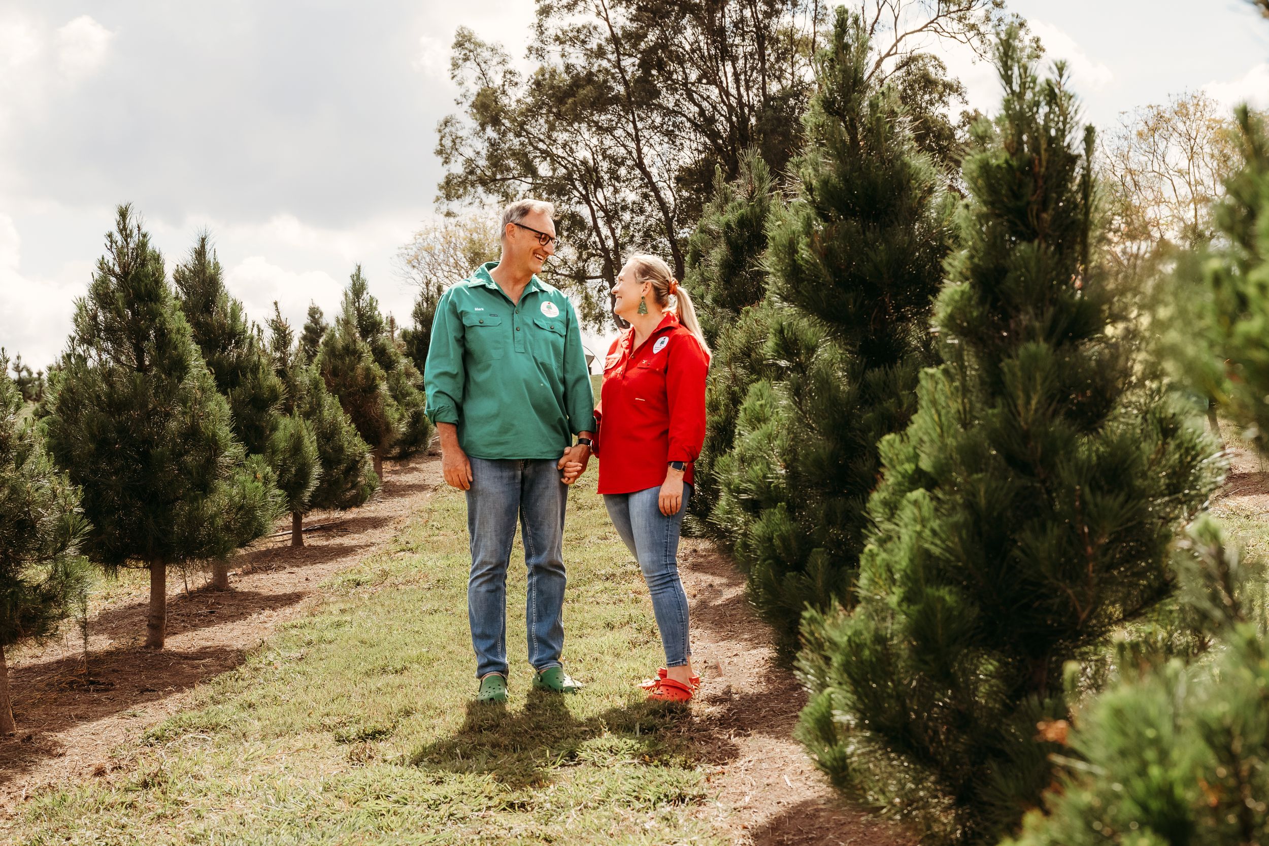 A couple walks together holding hands among rows of evergreen trees at a Christmas tree farm on an autumn day.