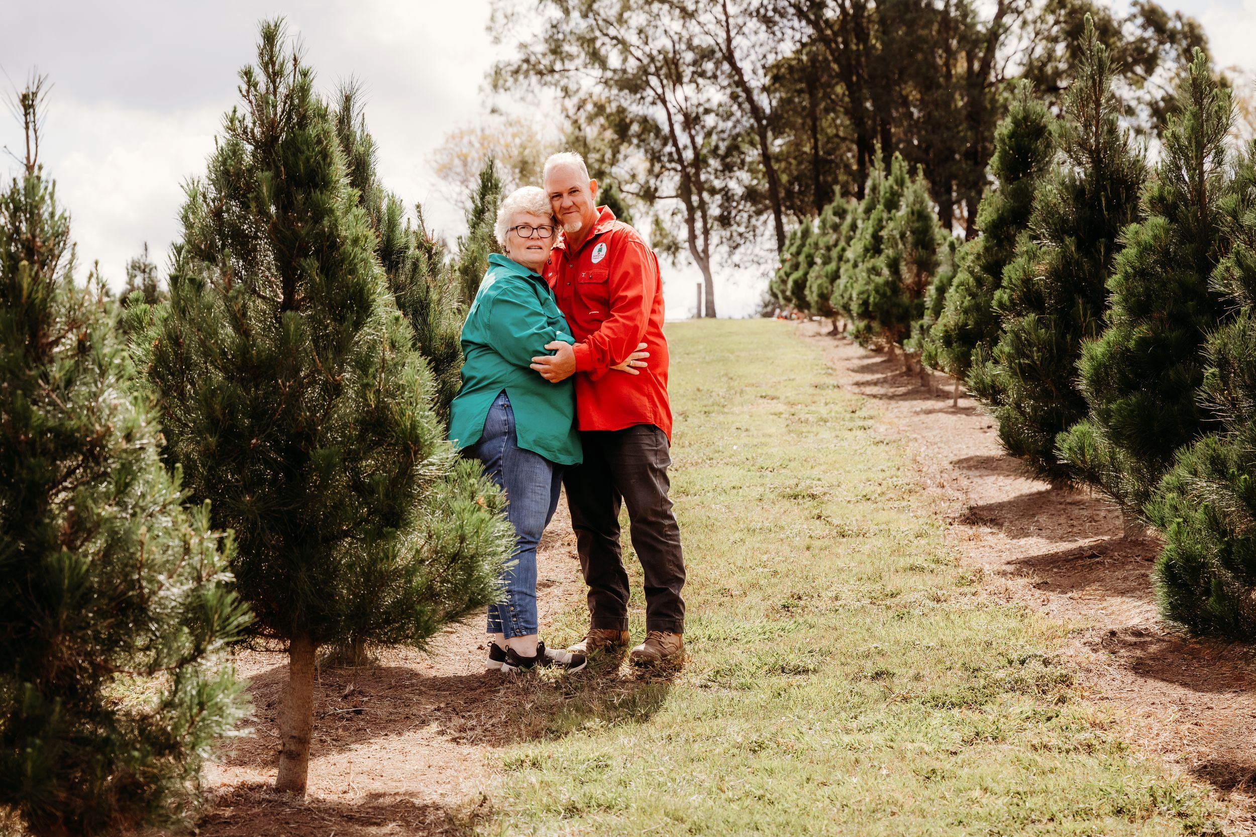Two people walk through rows of evergreen trees on a hill at a Christmas tree farm while browsing selections.
