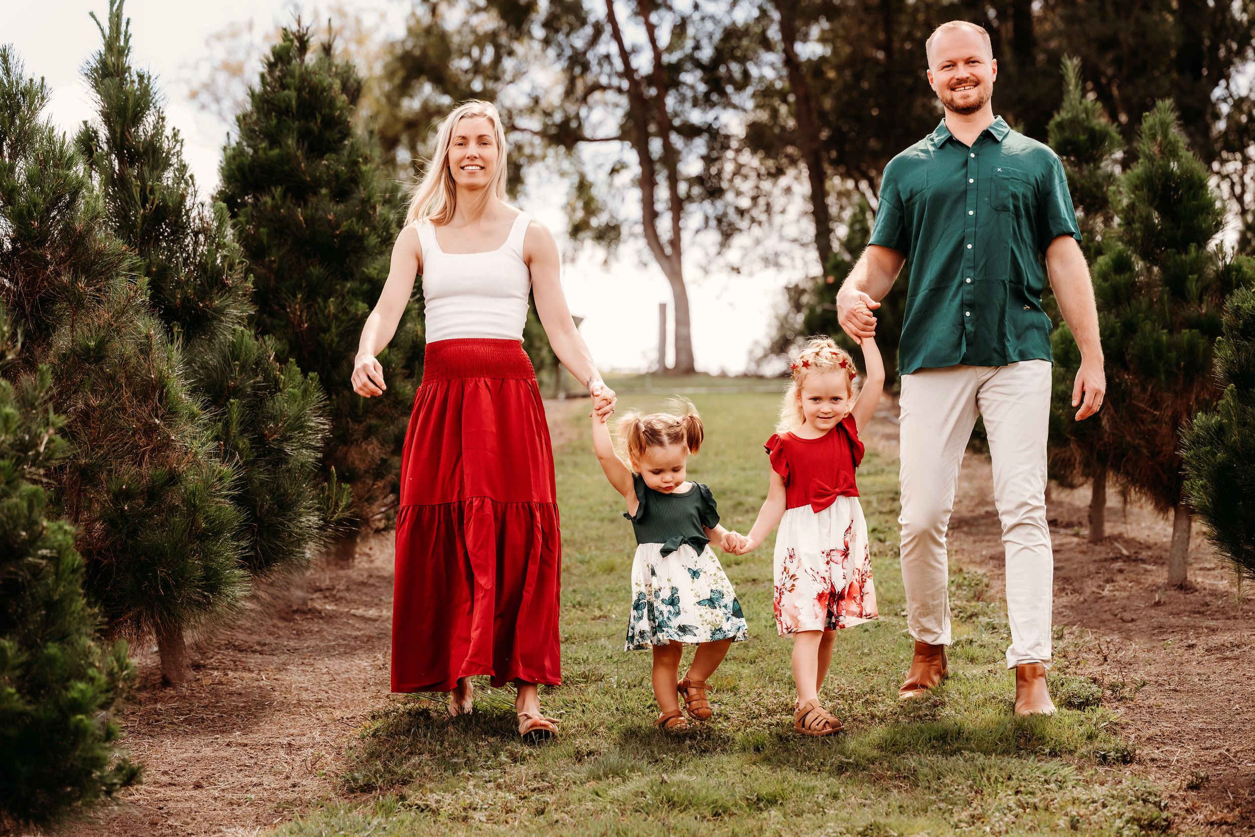 A family enjoying a casual outdoor photoshoot among pine trees wearing coordinated red and white outfits.