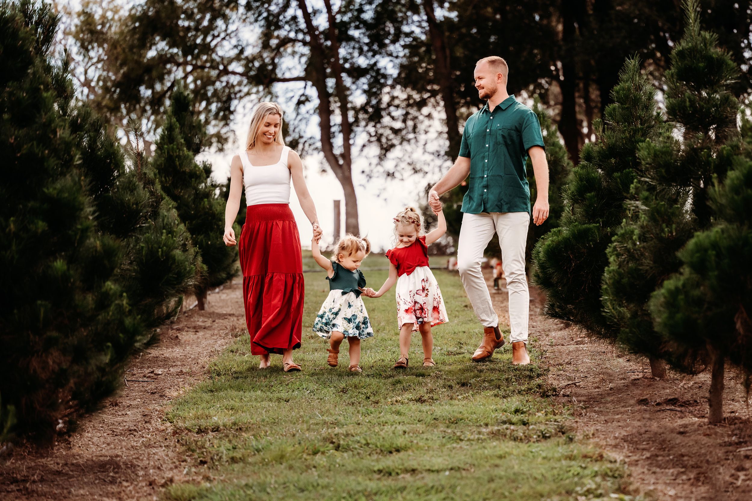 Group wearing red, black and white outfits walking among Christmas trees at a tree farm during winter season.