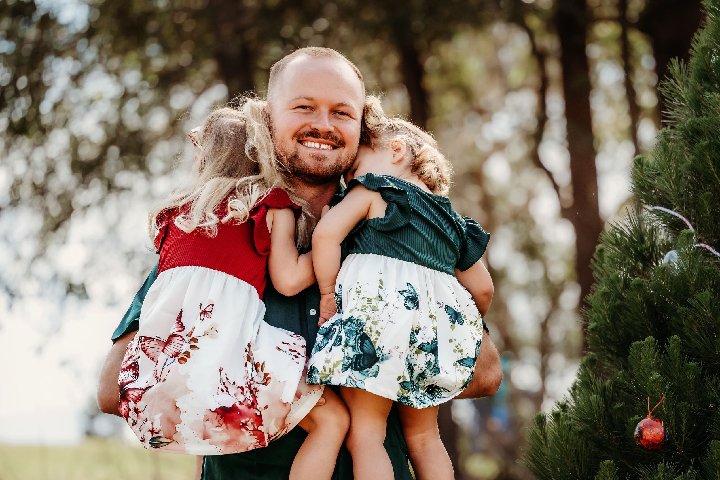 Family members share joyful embraces and laughter during an outdoor photo session in a wooded setting.