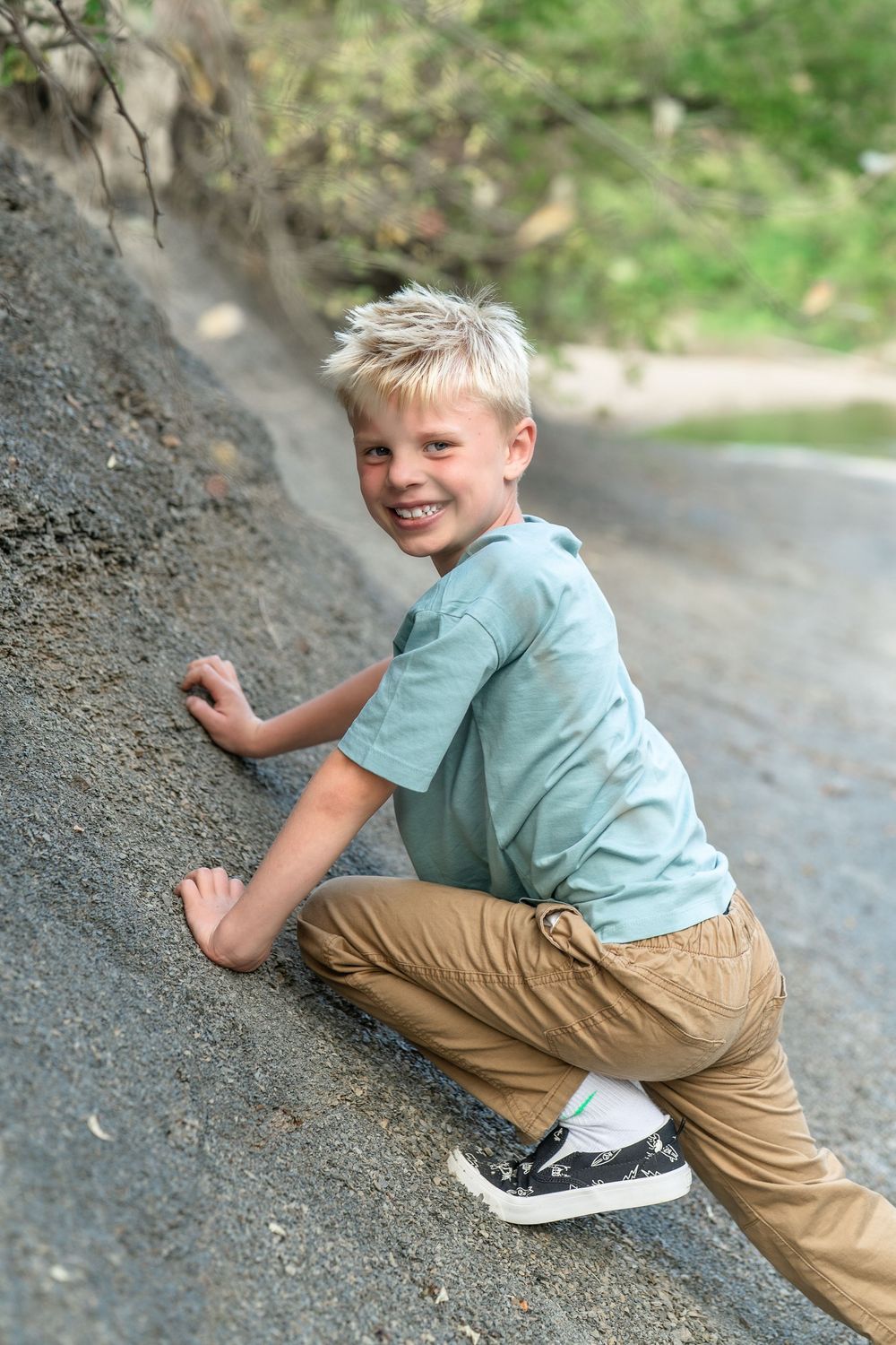 A child climbs on a sloped dirt embankment while wearing khaki pants and a teal t-shirt at Brecksville Reservation for a Family Session