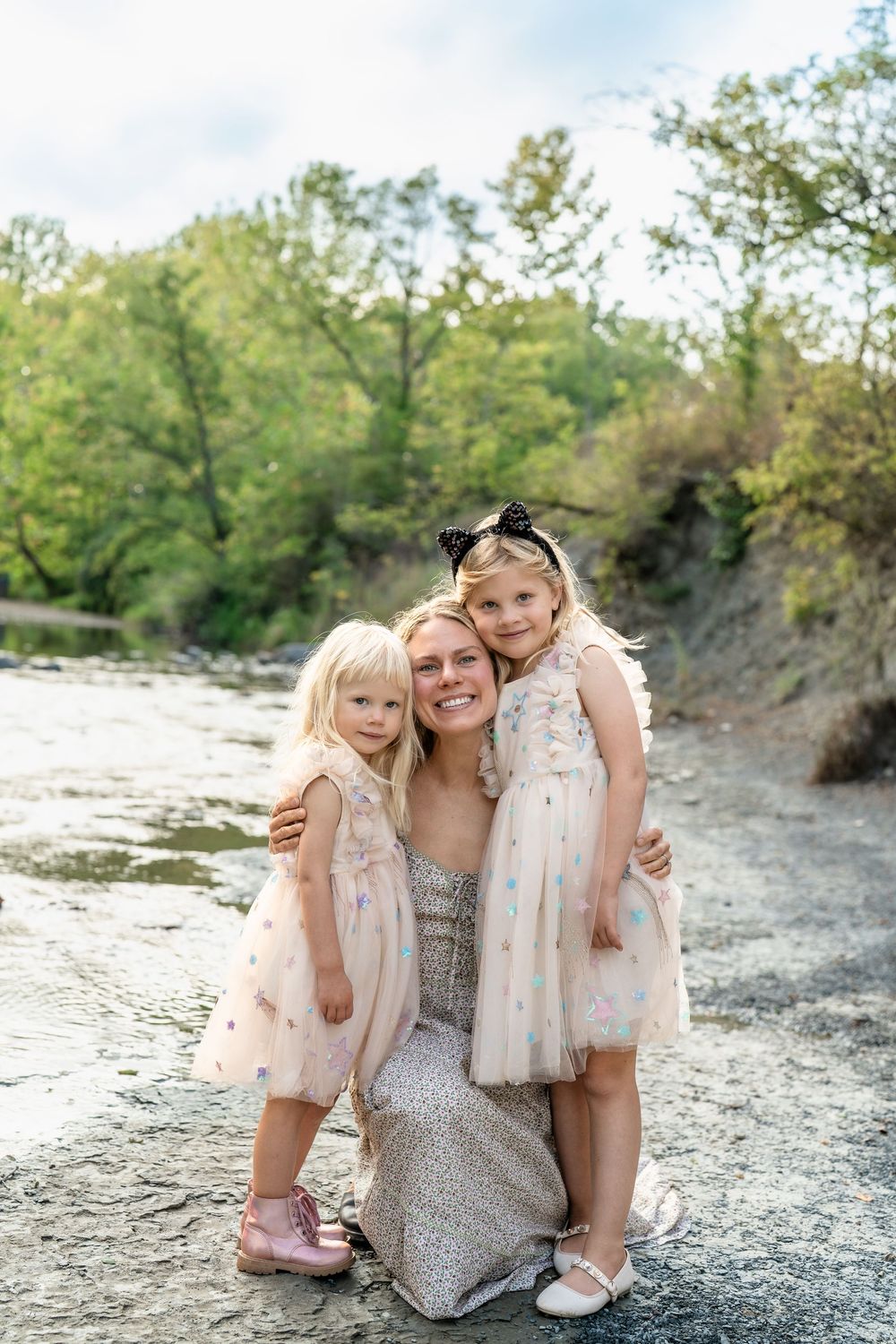 Family group poses together on rocky ground while wearing coordinated light-colored dresses among natural surroundings at Brecksville Park