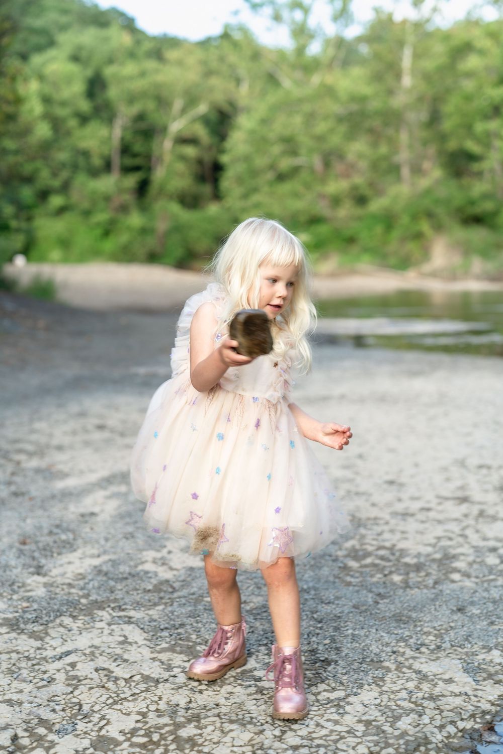 A small child in a pink tulle dress explores rocks along a riverbank at Brecksville Reservation in Cleveland, Ohio for Family Pictures.