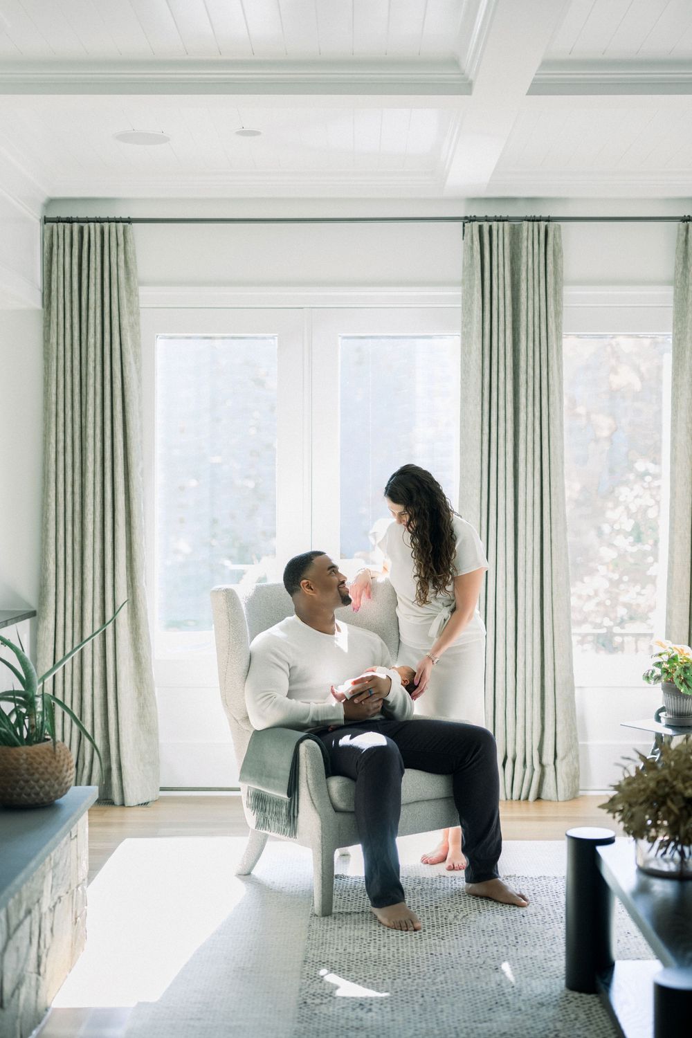 Two people sitting in a bright modern living room with mint green curtains and large windows.