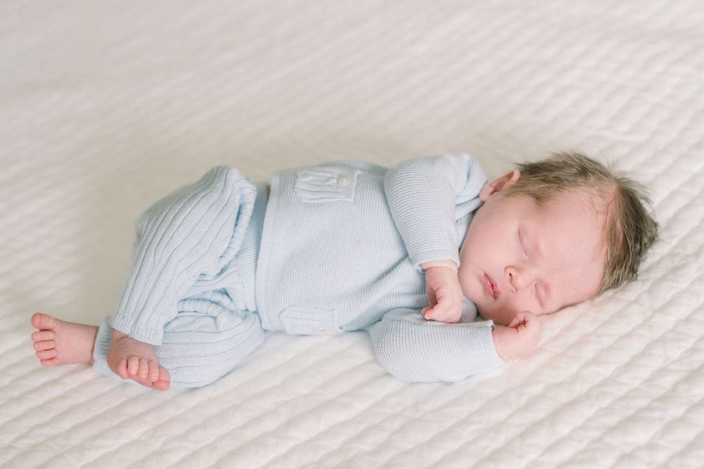 A sleeping baby wearing light blue pajamas lies peacefully on white bedding.