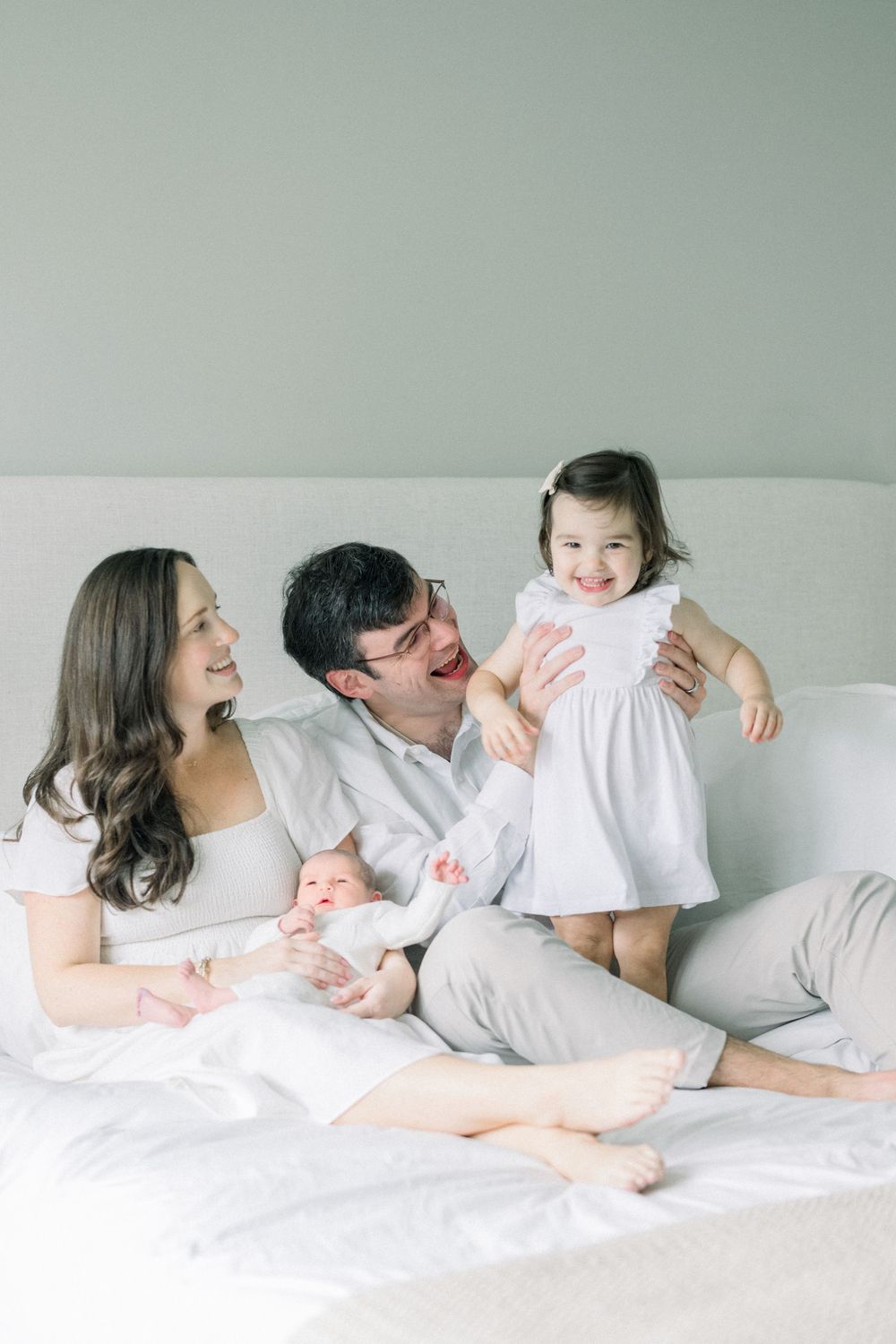 Family lying together on white bed sharing intimate moments in minimalist setting.