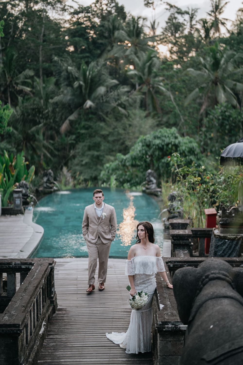 Newlyweds on wooden walkway by infinity pool surrounded by tropical palm trees in Bali.
