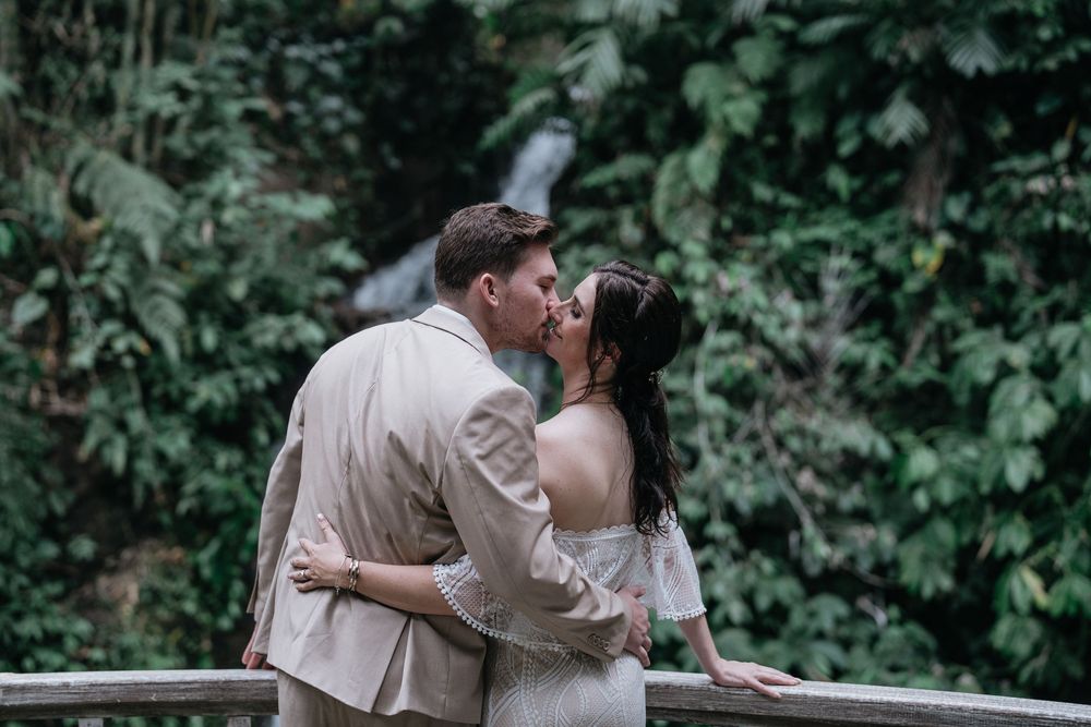 A couple embraces during their wedding photoshoot against a backdrop of tropical foliage.