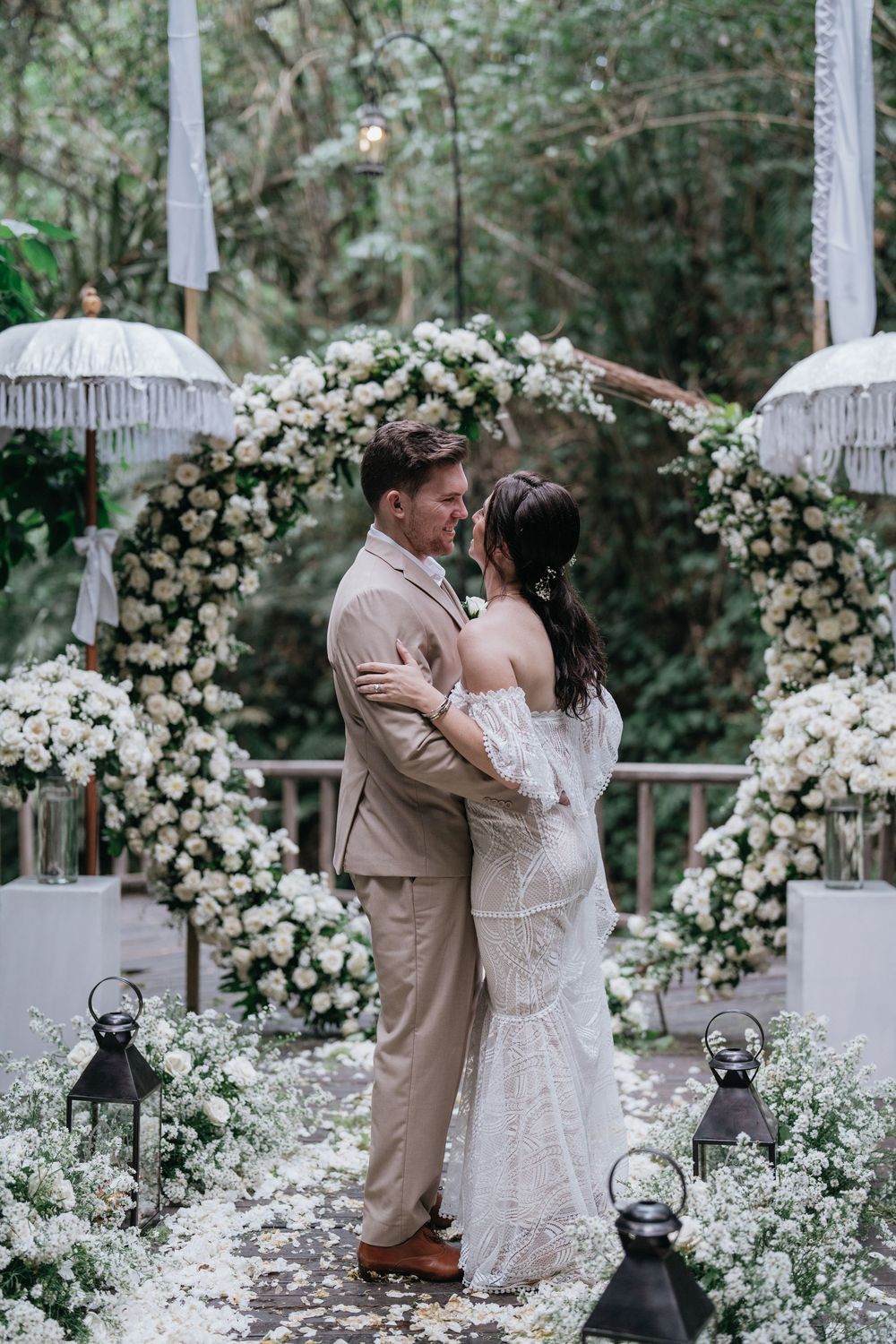 A romantic wedding scene with white floral arches and a couple sharing an intimate moment.