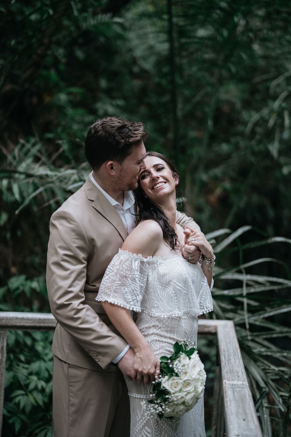 A couple shares joyful laughter during their wedding photoshoot in a tropical garden setting.