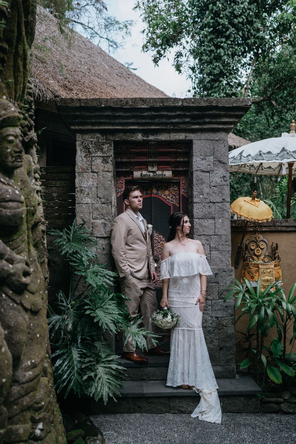 A couple poses in front of a rustic stone wall with tropical plants at their destination wedding.