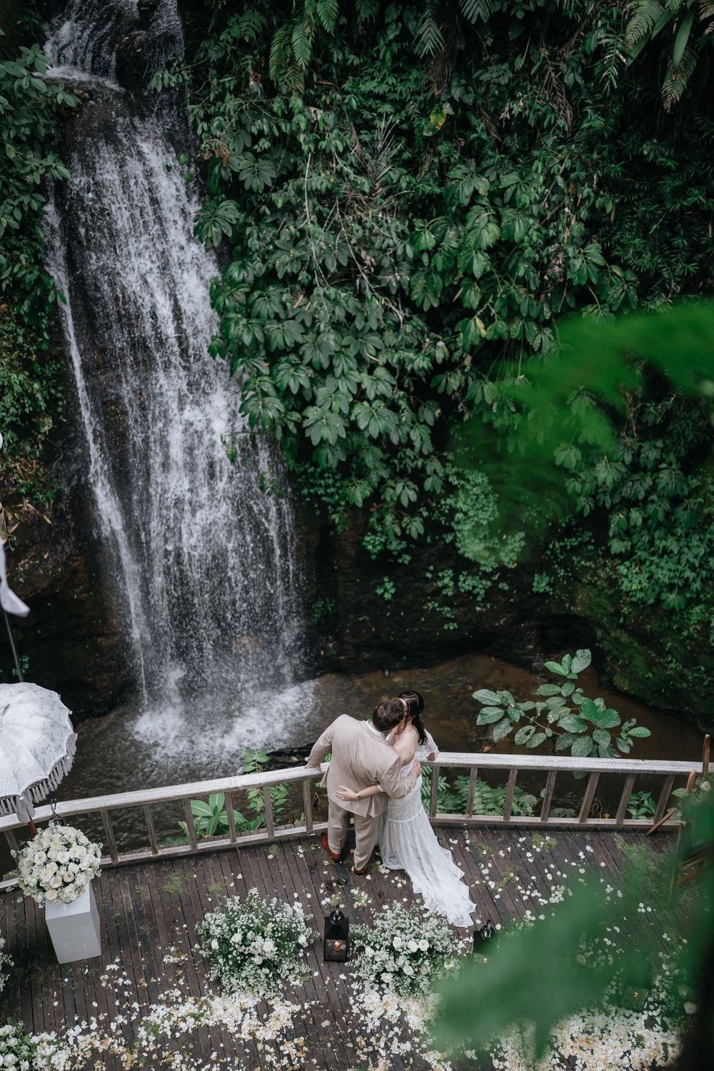 A wedding photoshoot by a scenic waterfall with white floral decorations.