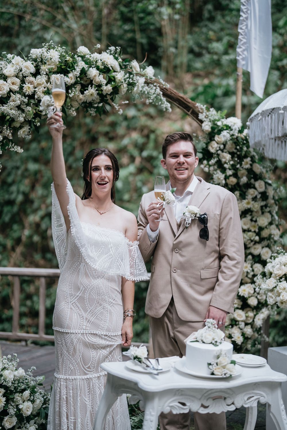A celebratory wedding toast moment with white floral decorations in the background.