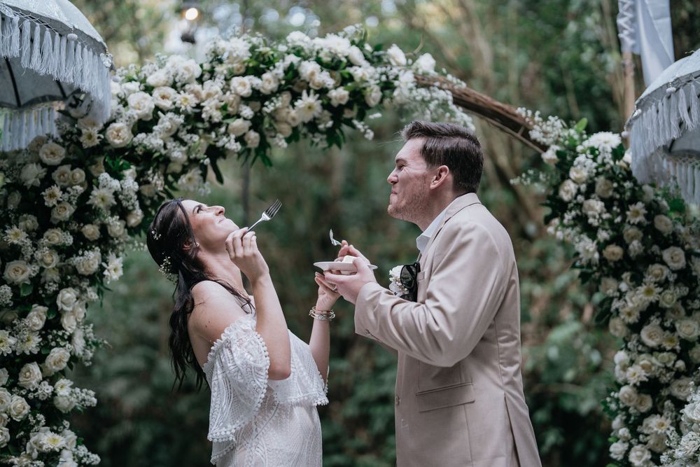 Romantic couple shares intimate moments under a floral archway during an outdoor wedding celebration.