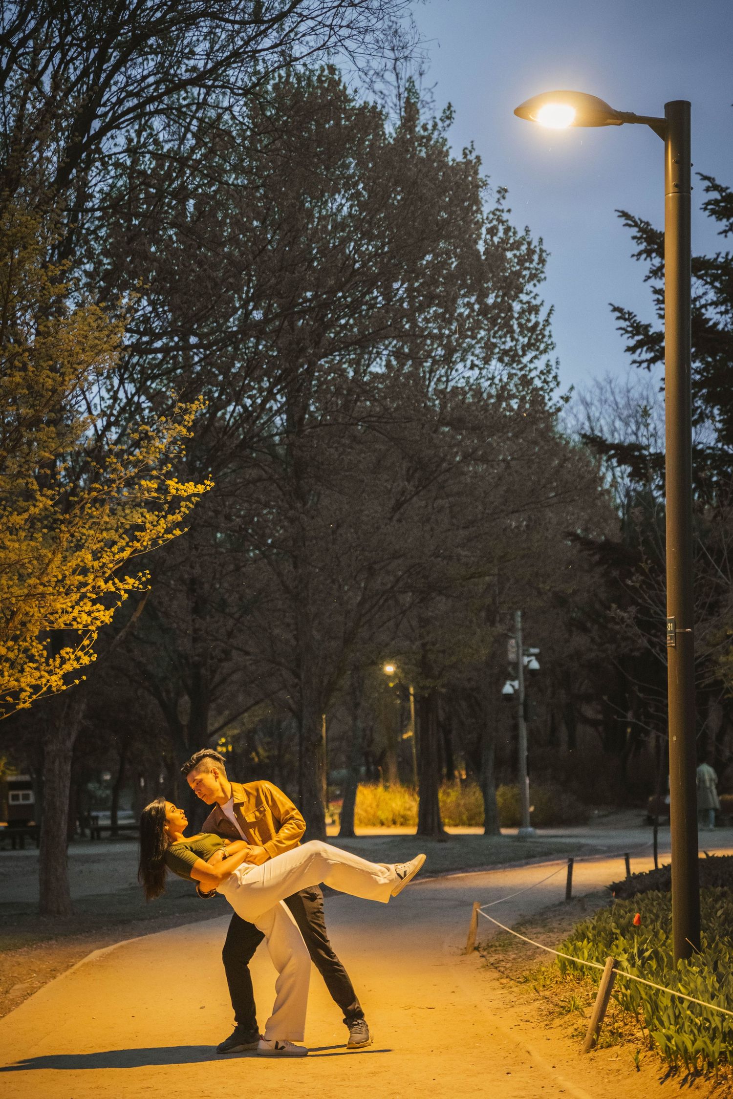 A sequence of photos showing a figure performing acrobatic moves under yellow street lights at night in a park.