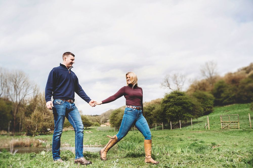 Person in jeans and boots kicking and splashing through a large puddle in a grassy field.