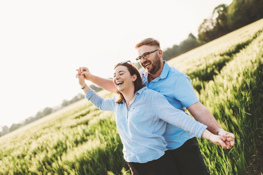A couple enjoys a romantic moment together in a sunny wheat field wearing casual summer attire.