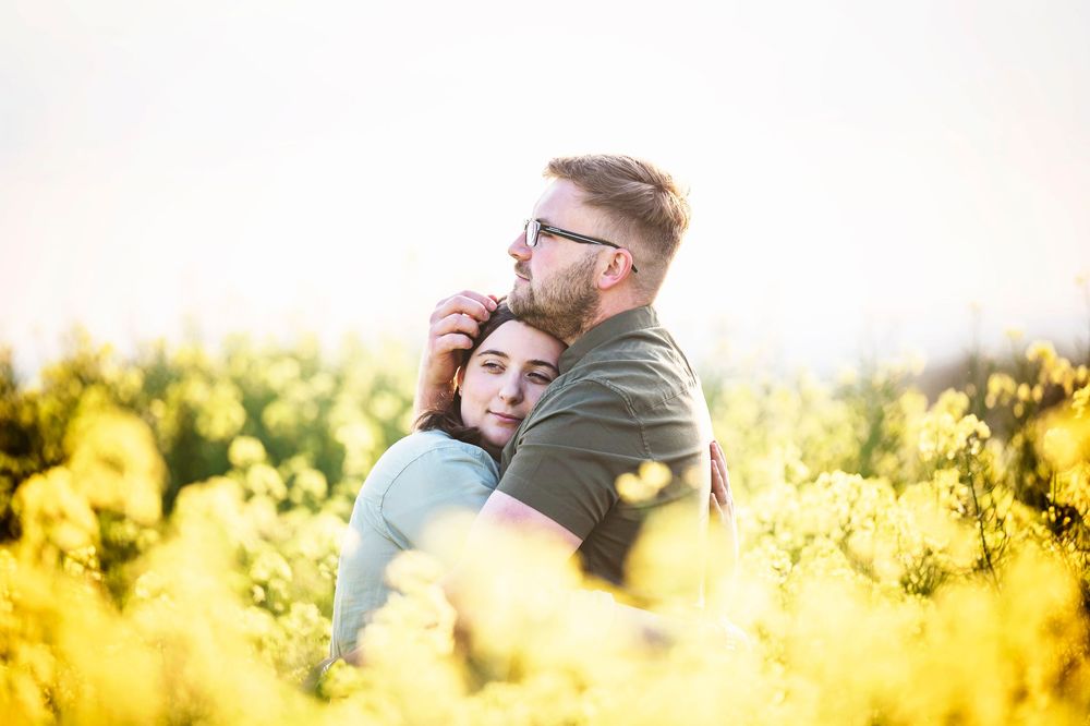 A warm golden sunlit field of yellow canola flowers with soft silhouettes of people in the foreground at sunset.