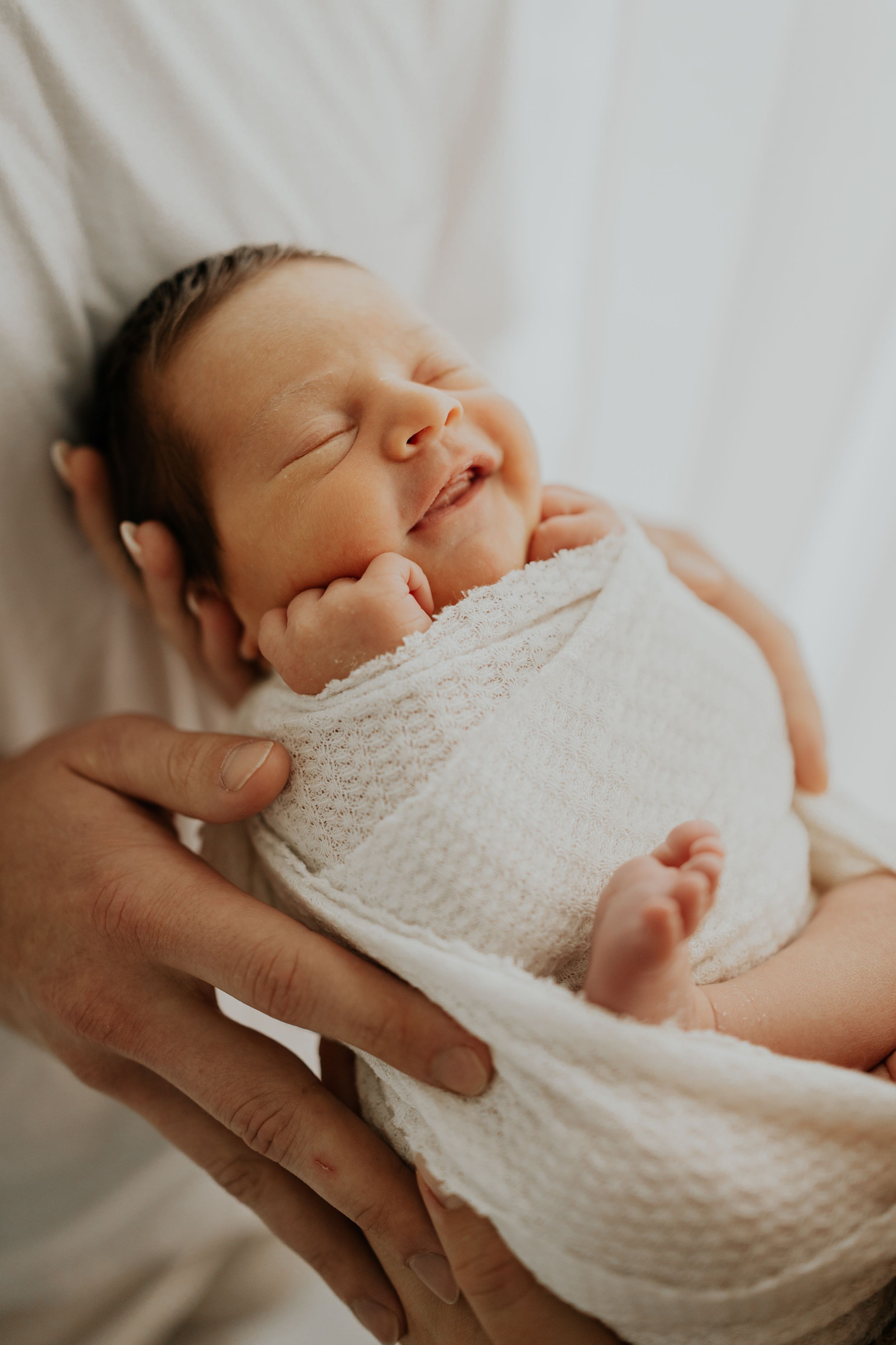 A series of peaceful newborn baby photos showing gentle hands holding an infant wrapped in soft white knitted blanket.