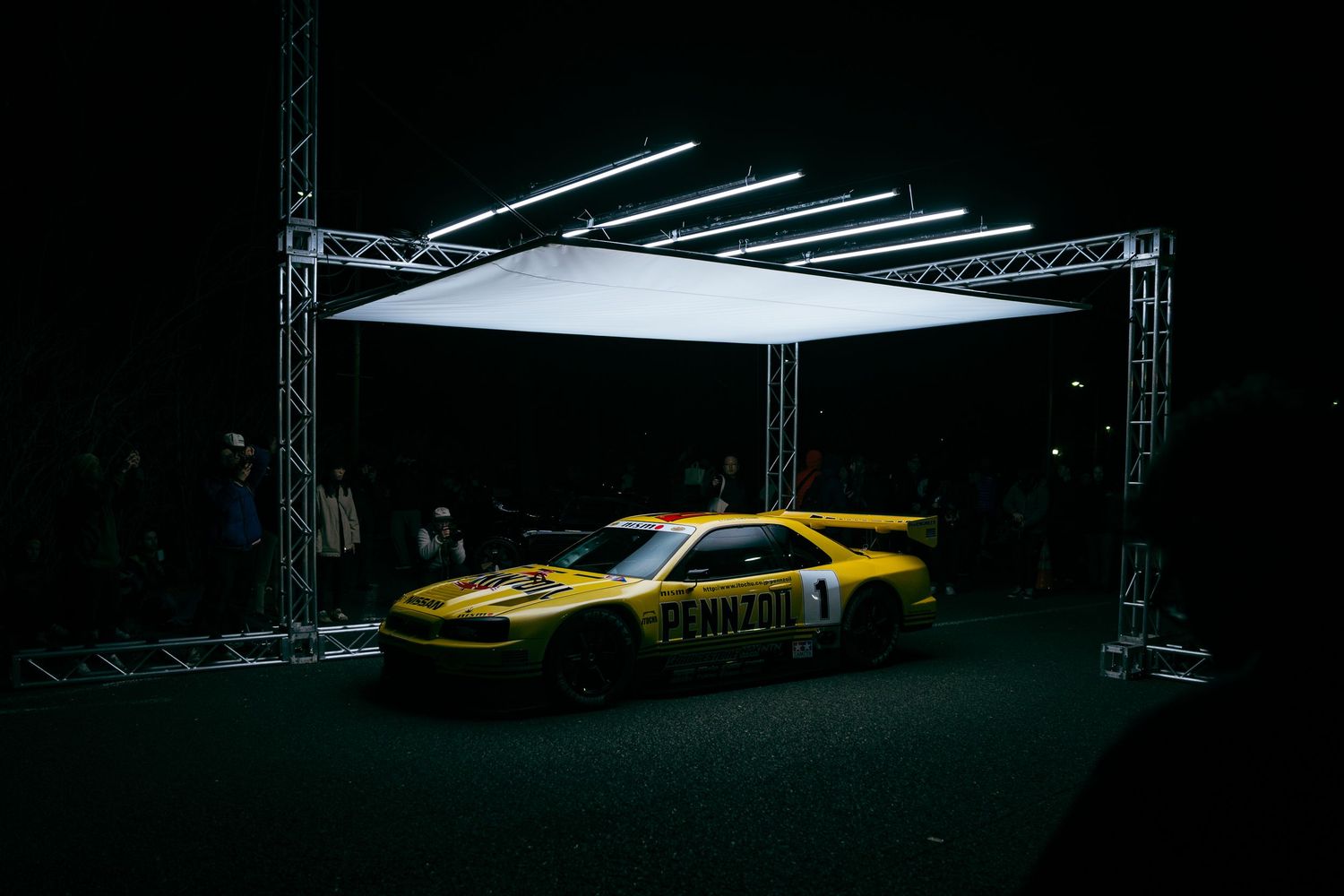 A dramatic low angle view of a yellow sports car with overhead lighting in a dark studio environment.