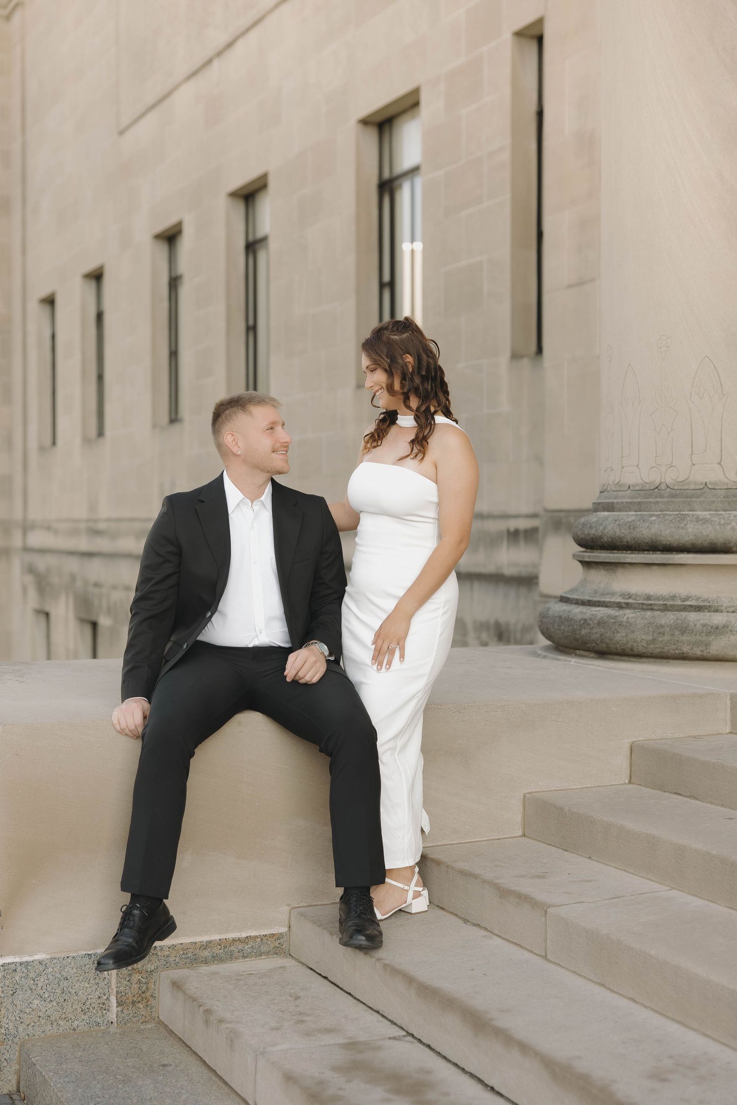 Elegant couple in wedding attire pose together on stone steps of a classic building exterior.