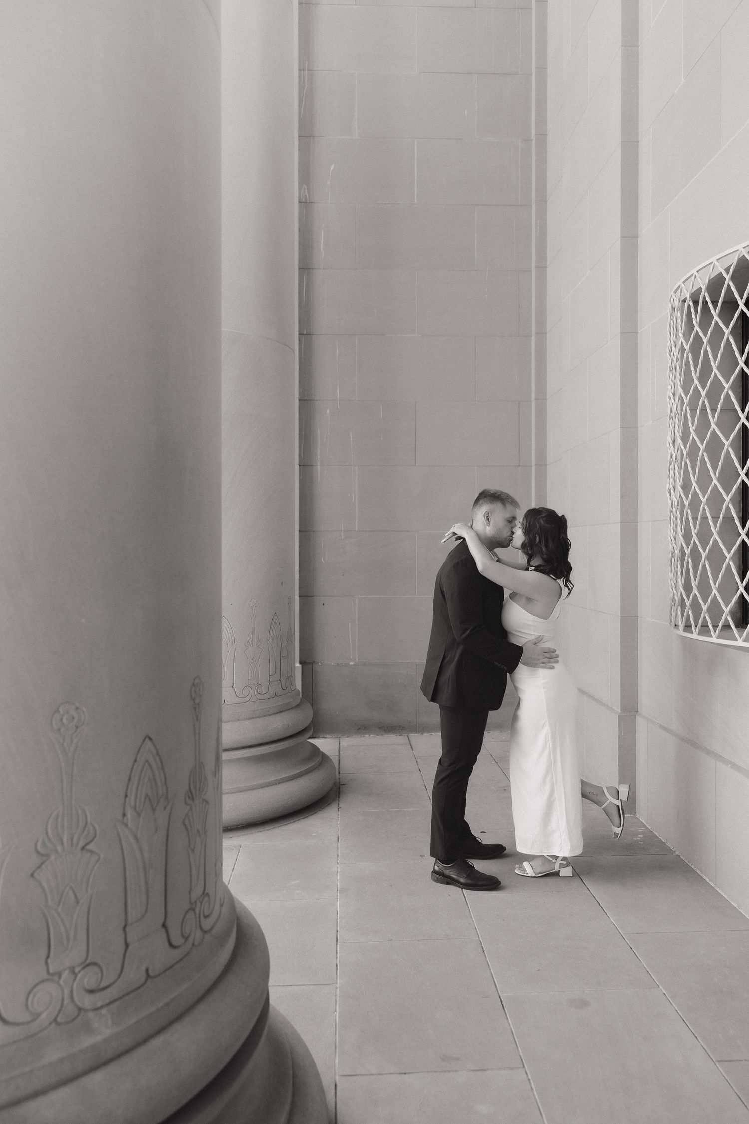A romantic wedding couple shares tender moments between classic white columns in a sequence of black and white photos.