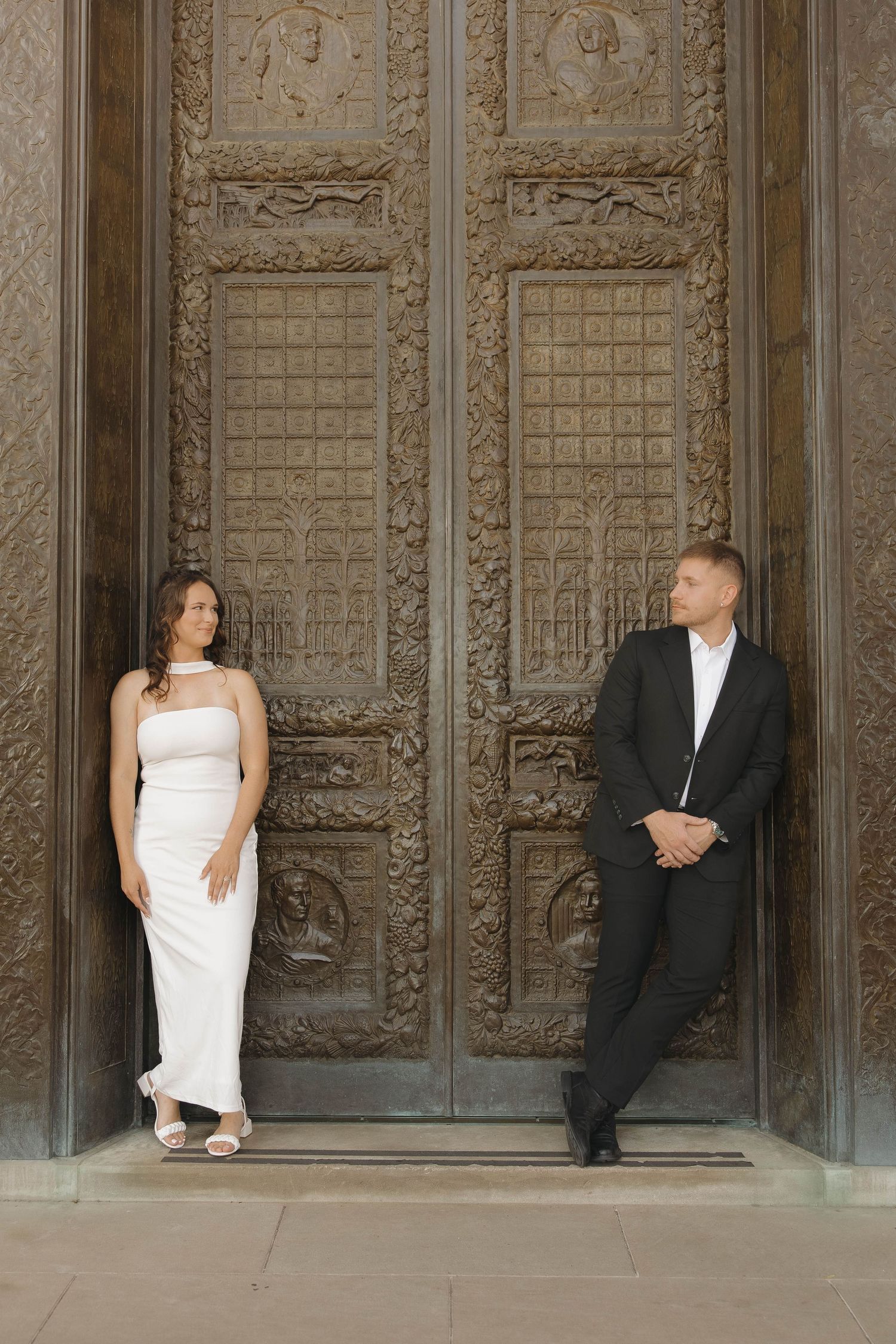 Creative wedding portrait shows couple posing artistically against ornate architectural columns.