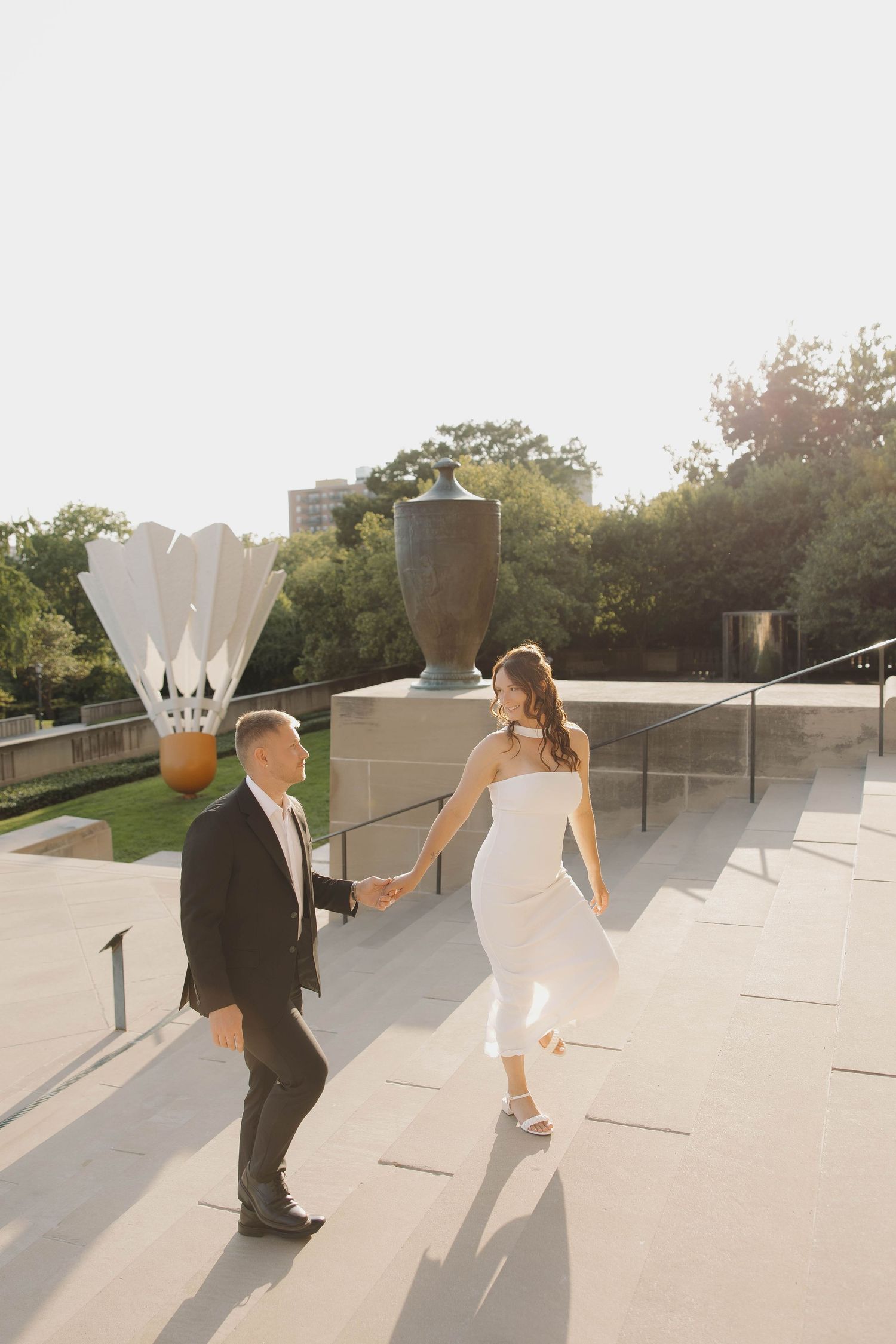 Couple in formal attire dances playfully on a sun-lit rooftop terrace during sunset.