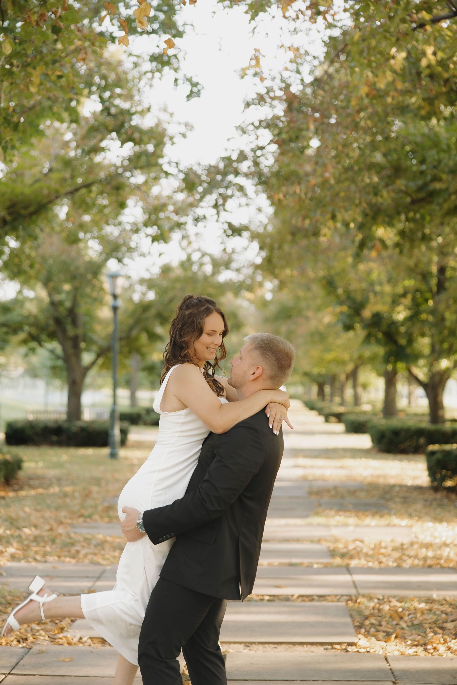 A romantic autumn wedding photo with fallen leaves in a park setting beneath golden trees.