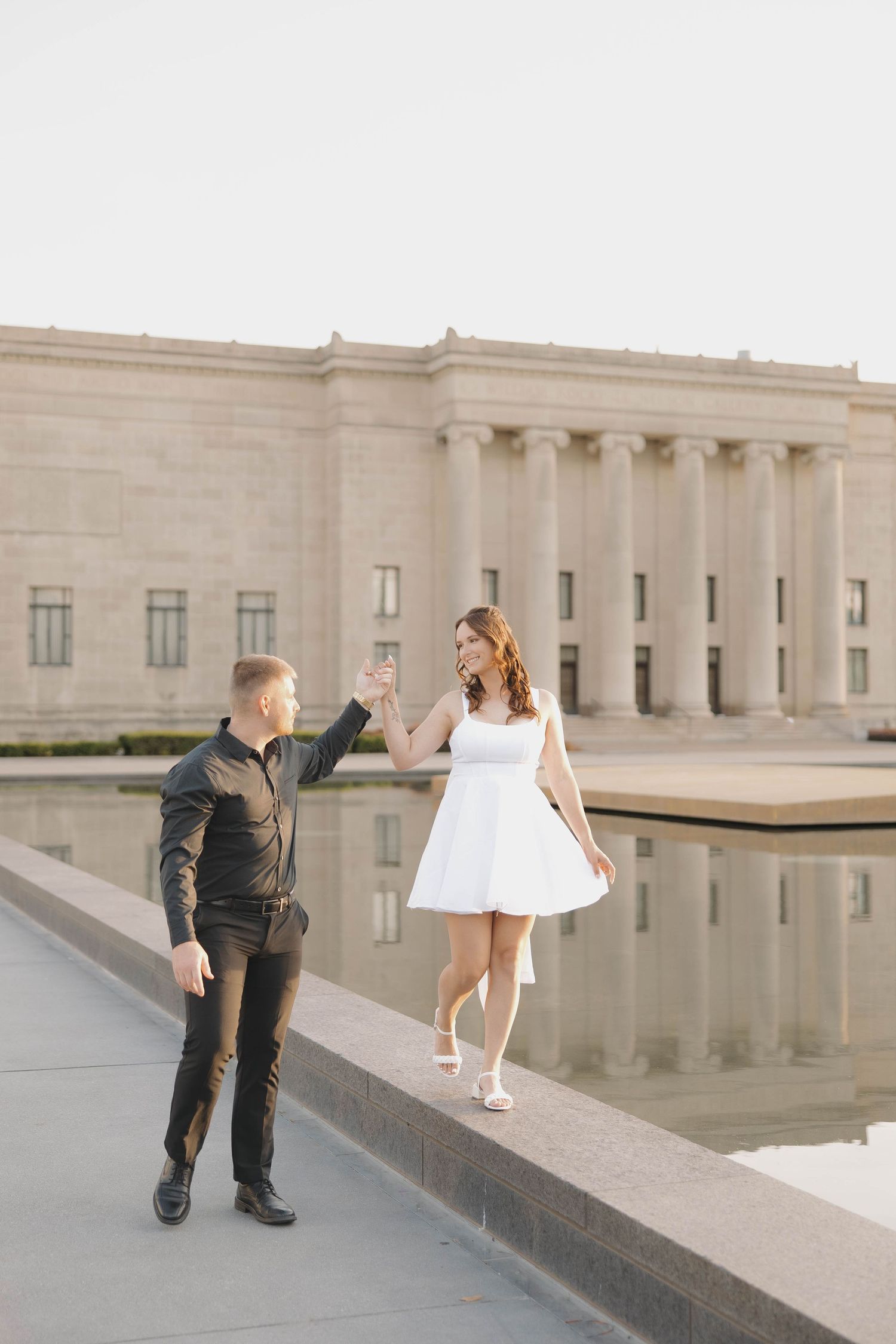 A romantic dance sequence unfolds between two people by a reflecting pool outside a grand stone building.