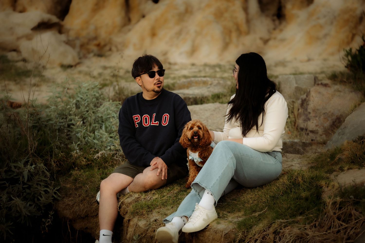 Couple sitting on rocks with a golden dog in a scenic outdoor setting, man wearing Polo Ralph Lauren sweatshirt.