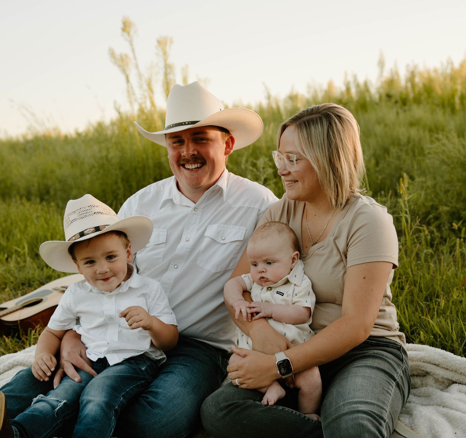 Family sitting together outdoors in a grassy field during golden hour.