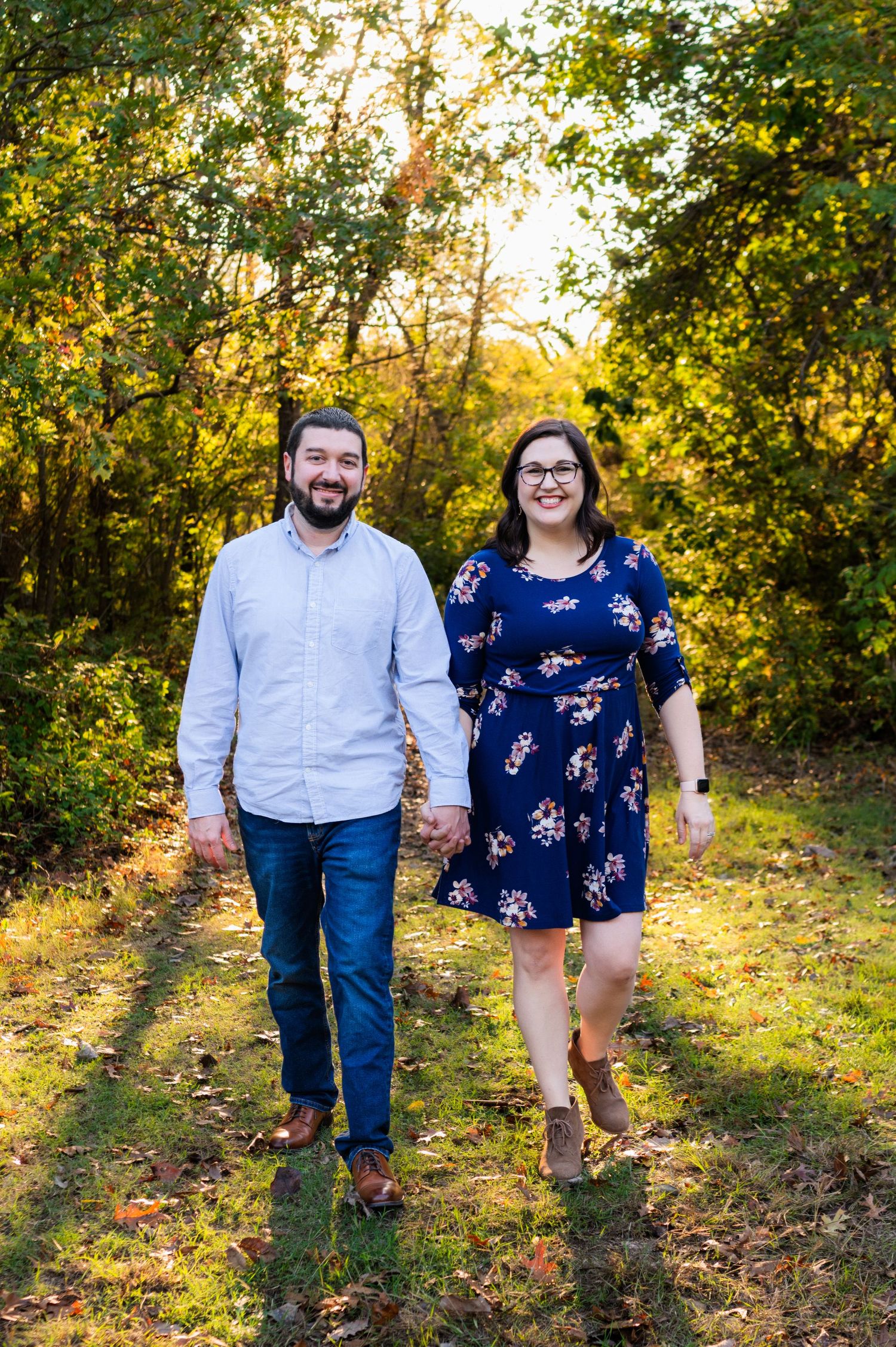 Mom and dad holding hands, smiling looking at camera and walking towards camera during fall family outdoor mini session close to sunset.